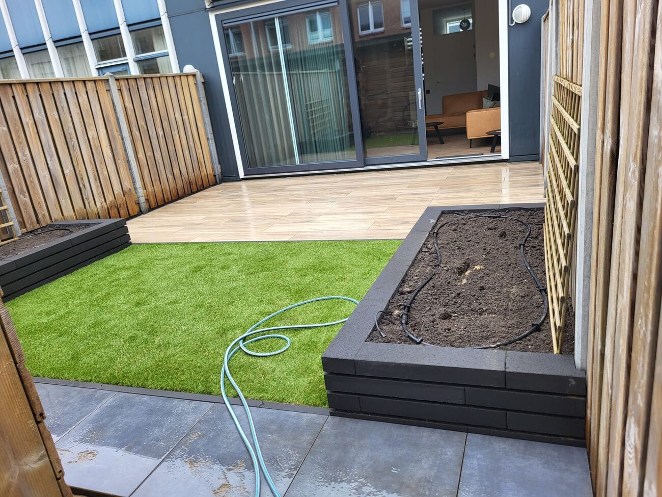 Achtertuin afgewerkt met kunstgras en plantenbak